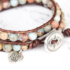 Genuine leather and beautiful Jasper stones that will remind you of a sunny beach, make up this gorgeous double wrap bracelet. Sand, dreamy light blue, and hints of rust swirl around in these stones and contrast nicely against a bold brown leather. 6mm (.62") diameter Aqua Terra Jasper gemstones Oval silver button, about 19mm (3/4") in width Rust brown leather Signature Bluefish logo heart charm 34 - 39 cm/13.5 - 15.5" length 2 button loop adjustments to fit most wrists Brown Natural Stone Wrap Bracelet Gift, Brown Spiritual Wrap Bracelet With Natural Stones, Spiritual Brown Wrap Bracelet With Natural Stones, Healing Brown Wrap Bracelet With Natural Stones, Bohemian Brown Wrap Bracelet With Natural Stones, Beaded Leather Wraps, Aqua Terra, Double Wrap Bracelet, Sunny Beach