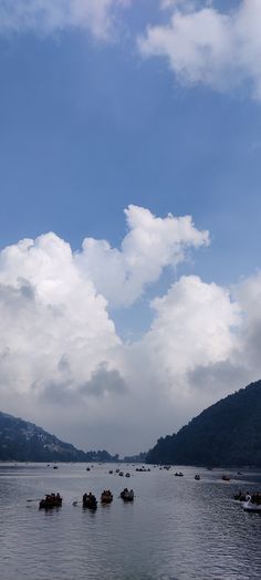 several small boats floating on top of a large body of water under a cloudy blue sky