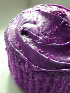 a cupcake with purple frosting sitting on a white plate