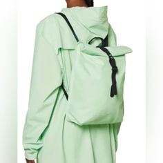 a woman wearing a green coat with a black backpack on her back and shoulder strap