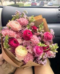 a woman holding a bouquet of pink and white flowers in her lap while sitting in the back seat of a car