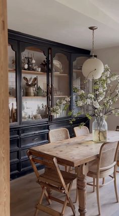 a dining room table with chairs and vases on it's side, in front of a china cabinet