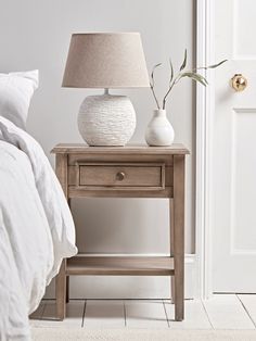 a white vase sitting on top of a wooden table next to a night stand with a lamp