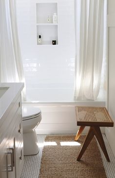 a white bathroom with a wooden bench in front of the toilet and shower curtained window