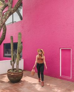 a woman in a straw hat walking past a pink building