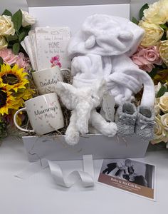 a white teddy bear sitting in a basket filled with baby's clothes and other items