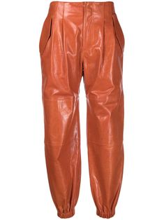 Laranja queimado, couro, detalhe de prega, acabamento elástico, modelagem cenoura, fechamento frontal oculto, dois bolsos laterais internos e dois bolsos posteriores com lapelas. Luxury Leather Bottoms With Pockets, Chic Orange Pleated Bottoms, Luxury High-waist Leather Pants With Pockets, Orange Trousers With Pockets, Luxury Orange Trousers, Orange Leather, Tapered Pants, Pleated Pants