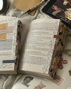 an open book sitting on top of a bed next to a clock and other items