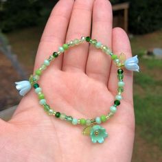 Add a touch of whimsy to your outfit with our bracelet featuring vibrant green glass beads and three dainty iridescent flowers! A stylish and practical gift for anyone who loves handmade accessories and unique fashion statements. Treat yourself or someone special today! One size fits most. Made with glass beads and plastic charms. Ships within 3-5 business days. Want a different color variation? Send us a message! We love creating custom pieces to suit your personal style. Green Bracelet With Flower Charm As Gift, Green Beaded Flower Crystal Bracelet, Green Beaded Bracelets With Flower Charm For Gift, Bohemian Green Bracelets With Flower Charm, Green Bohemian Beaded Bracelets For Spring, Green Charm Bracelet With Colorful Beads As Gift, Adjustable Green Bracelets With Flower Charm, Adjustable Spring Crystal Bracelet With Flower Shape, Green Bracelets For Spring Gift