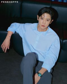 a man sitting on top of a black couch wearing a blue shirt and grey pants