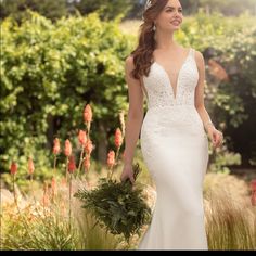 a woman in a wedding dress is walking through some tall grass and holding a bouquet