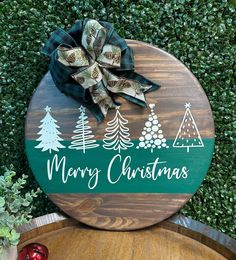 a wooden sign that says merry christmas with trees and evergreens on the front, sitting on top of a barrel