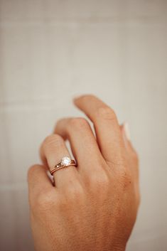 a woman's hand wearing a gold ring with a small white diamond on it