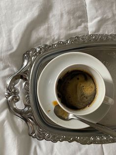 a cup of coffee is sitting on a silver tray with a spoon and saucer