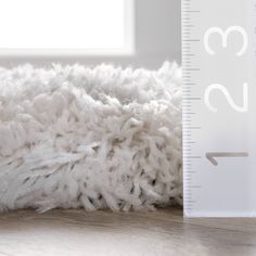 a white rug is next to a ruler on the floor in front of a window