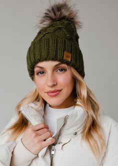 a woman wearing a green hat with fur pom - poms on it's head