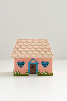 a small pink house with blue windows and hearts on the roof is sitting on a white surface