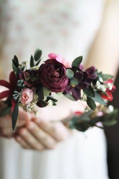 a woman holding flowers in her hands while wearing a white dress and red flower crown