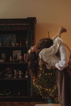 a man and woman are kissing in front of a christmas tree with lights on it