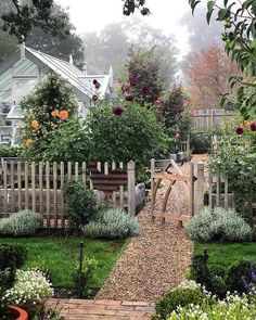 a garden with lots of plants and flowers around it, including roses on the fence