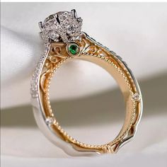 a diamond and emerald ring sitting on top of a white cloth