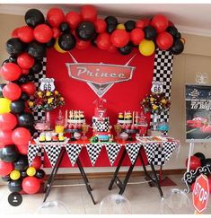 a table topped with lots of balloons next to a red and black sign that says prince