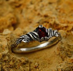 a silver ring with a red stone in the middle on top of some rocks and dirt