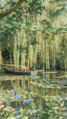 a small boat floating on top of a lake surrounded by lily pads and willow trees