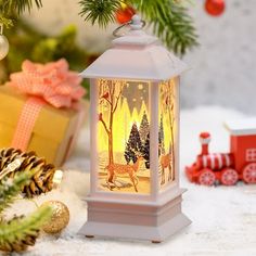 a white lantern sitting on top of a snow covered ground next to christmas decorations and presents