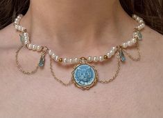 **Vintage-Inspired Cat Cameo Pearl Choker Necklace** Elevate your accessory collection with this exquisite, handcrafted choker necklace, featuring a charming vintage-inspired cat cameo at its center. The cameo, set in a delicate gold-toned frame, showcases an adorable blue-hued feline design, making it a perfect gift for cat lovers and vintage jewelry enthusiasts alike. This unique piece is adorned with lustrous faux pearls and accented with gold beads, adding a touch of elegance. The choker is Cameo Choker, Crystal Pendants, Cameo Jewelry, Pearl Choker Necklace, Choker Style, Fancy Jewelry, Pearl Choker, Blue Crystals, Gold Beads