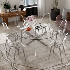 a glass table with chairs around it in front of a couch and coffee table near a window