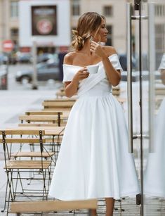 a woman in a white dress standing next to a table with chairs and tables behind her