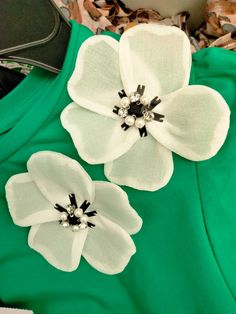 two white flowers are on top of a green shirt with black and white trims