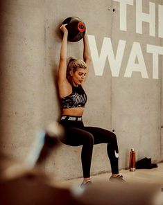 a woman is doing squats with a kettle on her back and the wall behind her