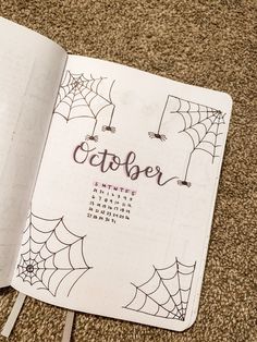 an open notebook with the word october written on it and spider webs in the background