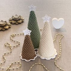 three knitted christmas trees sitting on top of a table next to beads and decorations