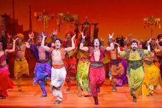 a group of men and women in colorful costumes on stage with their hands up to the sky