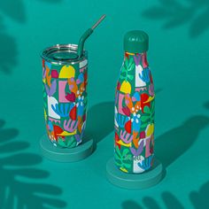 two colorful tumblers sitting next to each other on a blue surface with leaves and flowers