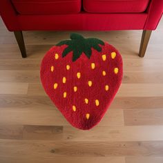 a strawberry shaped rug on the floor in front of a red couch with yellow dots