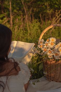 a woman reading a book while holding a basket with daisies