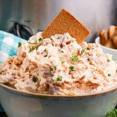 a bowl full of chicken salad with crackers on the side and bread in the background