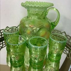 a green glass pitcher and six glasses on a table