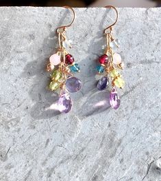 "Gemstone Dangle Earrings Cluster Earrings in Gold Fill Pink amethyst briolettes drop from shimmering gold fill, accompanied by a glorious cluster of tiny gemstones: Garnet, Iolite, Peridot, Rose Quartz, Fluorite, and London Blue Topaz. Lavishly wrapped in gold-filled wire, the genuine gemstones twinkle and sparkle fetchingly. Wire-wrapped to a paperclip link gold-filled chain, the earrings dangle from ball-tipped earring wires. Also available in lever back earring wires, which snap shut for gre Gemstone Accented Dangle Earrings, Multicolor Dangle Earrings With Gemstone Accents, Multicolor Gemstone Accented Drop Earrings, Multi-stone Dangle Earrings For Party, Multicolor Multi-stone Dangle Earrings, Dangle Crystal Earrings With Gemstone Accents As Gift, Dangle Multi-stone Earrings For Gifts, Long Drop Multi-stone Earrings For Gift, Multi-stone Long Drop Jewelry Gift