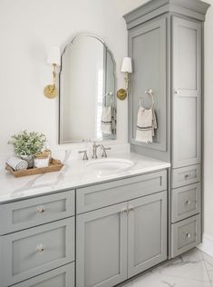 a bathroom with gray cabinets and white marble counter tops, gold accents on the mirror