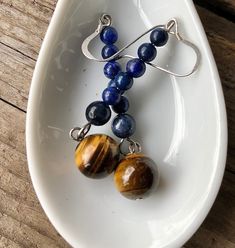 Charming blue Lapis Lazuli and gold Tiger Eye earrings are stunning. These cool 2.25 inch earrings are elegant enough that they would Step up your style game with these stunning earrings, featuring a gorgeous combination of Tiger Eye and Lapis Lazuli. The natural earthy tones of the gemstones make these earrings a versatile accessory that can be dressed up or down, depending on the occasion. With their sophisticated design, these earrings are perfect for a formal setting, but also versatile enou Blue Spiritual Earrings For Gifts, Spiritual Blue Jewelry For Birthday, Spiritual Blue Jewelry For Birthdays, Blue Dangle Earrings For Mother's Day, Blue Jewelry With Matching Earrings For Mother's Day, Spiritual Blue Jewelry For Mother's Day, Blue Dangle Jewelry For Birthday, Blue Dangle Jewelry For Mother's Day, Earrings Handmade Boho