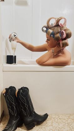 a woman sitting in a bathtub with hair curls on her head and two pairs of black cowboy boots