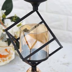 a glass candle holder sitting on top of a white table next to flowers and a vase