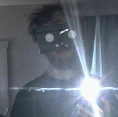 a man wearing a mask and holding a light up in front of his face while looking at the camera