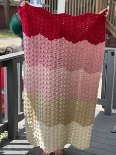 a woman holding up a crocheted blanket on top of a wooden porch railing