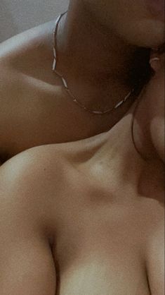 a close up of a woman with no shirt on laying down and wearing a necklace